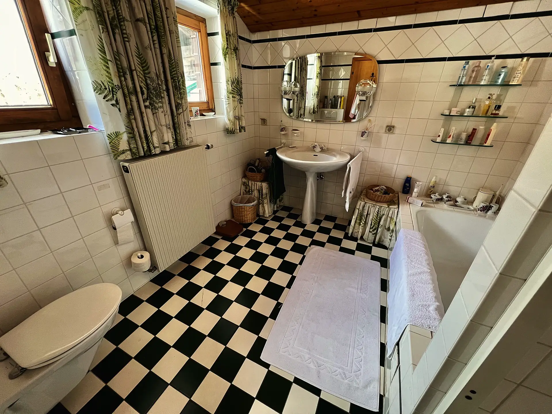 Badezimmer mit schwarz-weiß kariertem Fliesenboden, Standwaschbecken, ovalem Spiegel und Badewanne.