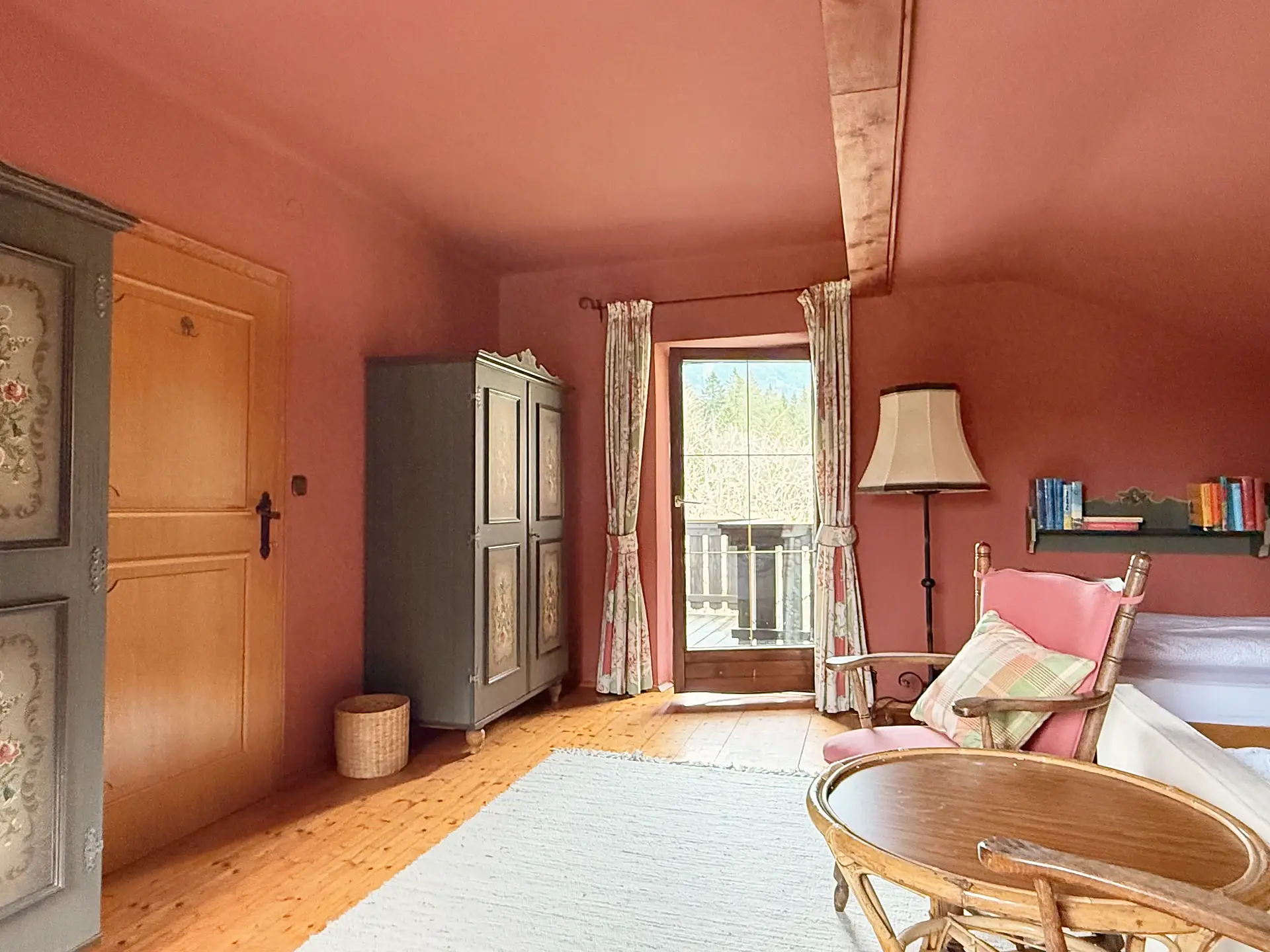 Gleiches Zimmer mit grau bemaltem Bauernschrank und Balkontür.