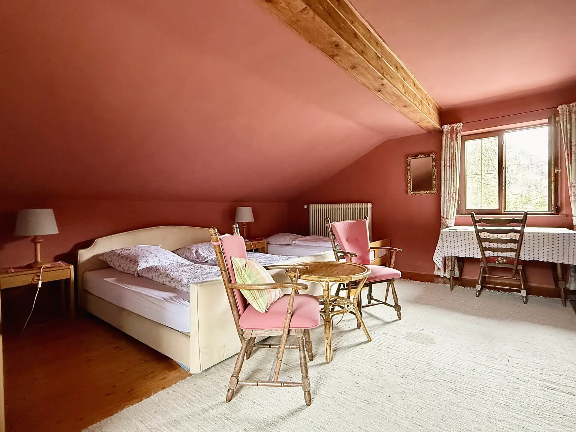 Das Viererzimmer unter dem Dach: altrosa gestrichene Wände, Doppelbett, Einzelbett und rosa Polsterstühle um einen runden Tisch.