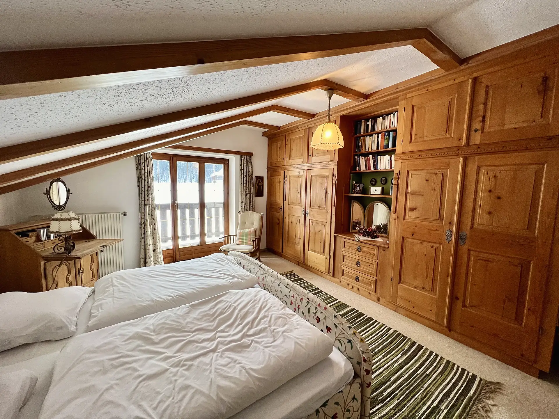 Gleiches Dachzimmer mit Blick auf Bücherregal, Kommode und Fenster.