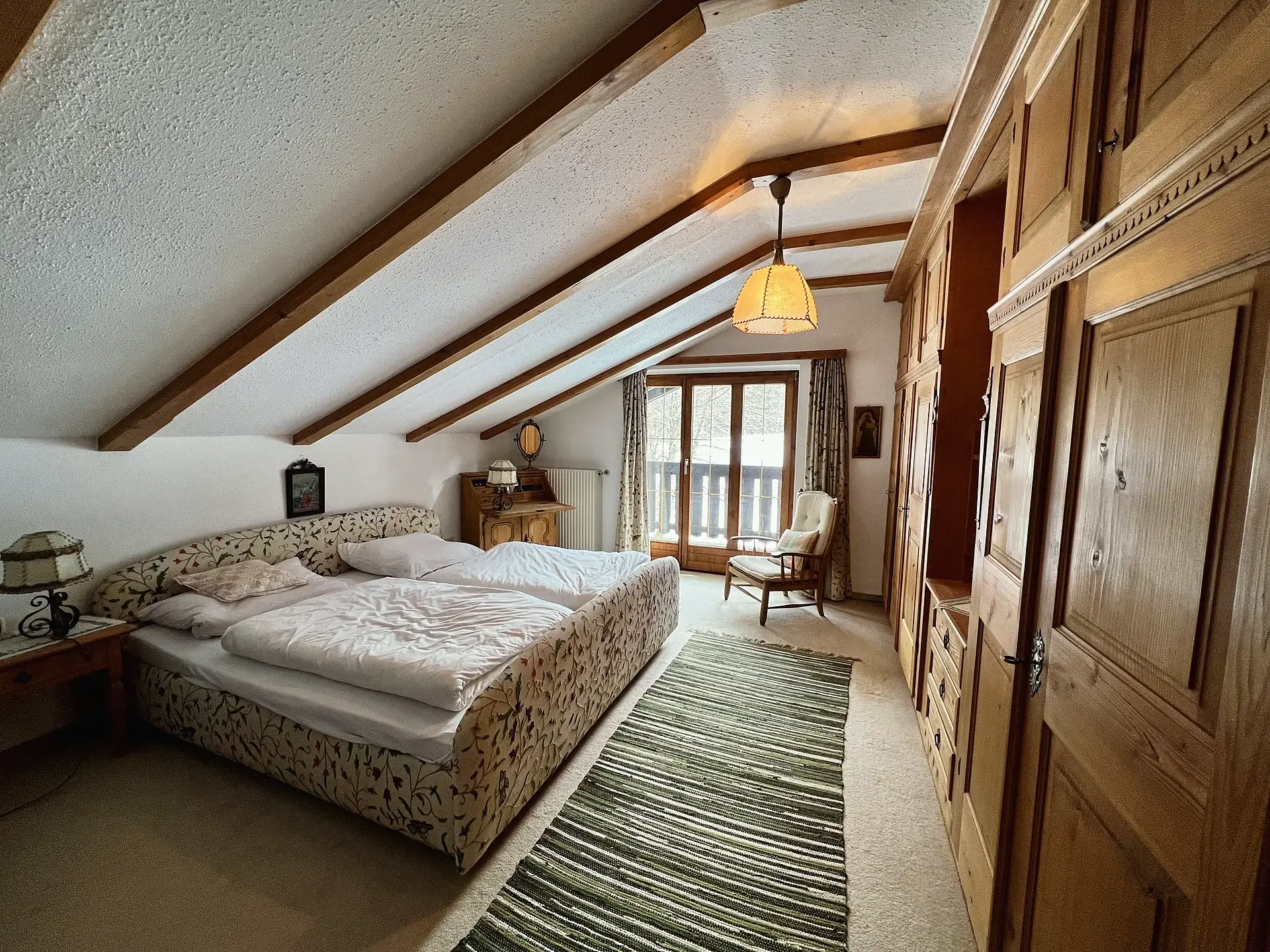 Zimmer unter dem Dach mit Doppelbett, gemustertem Kopfteil und einer Wand aus Holz-Einbauschränken.