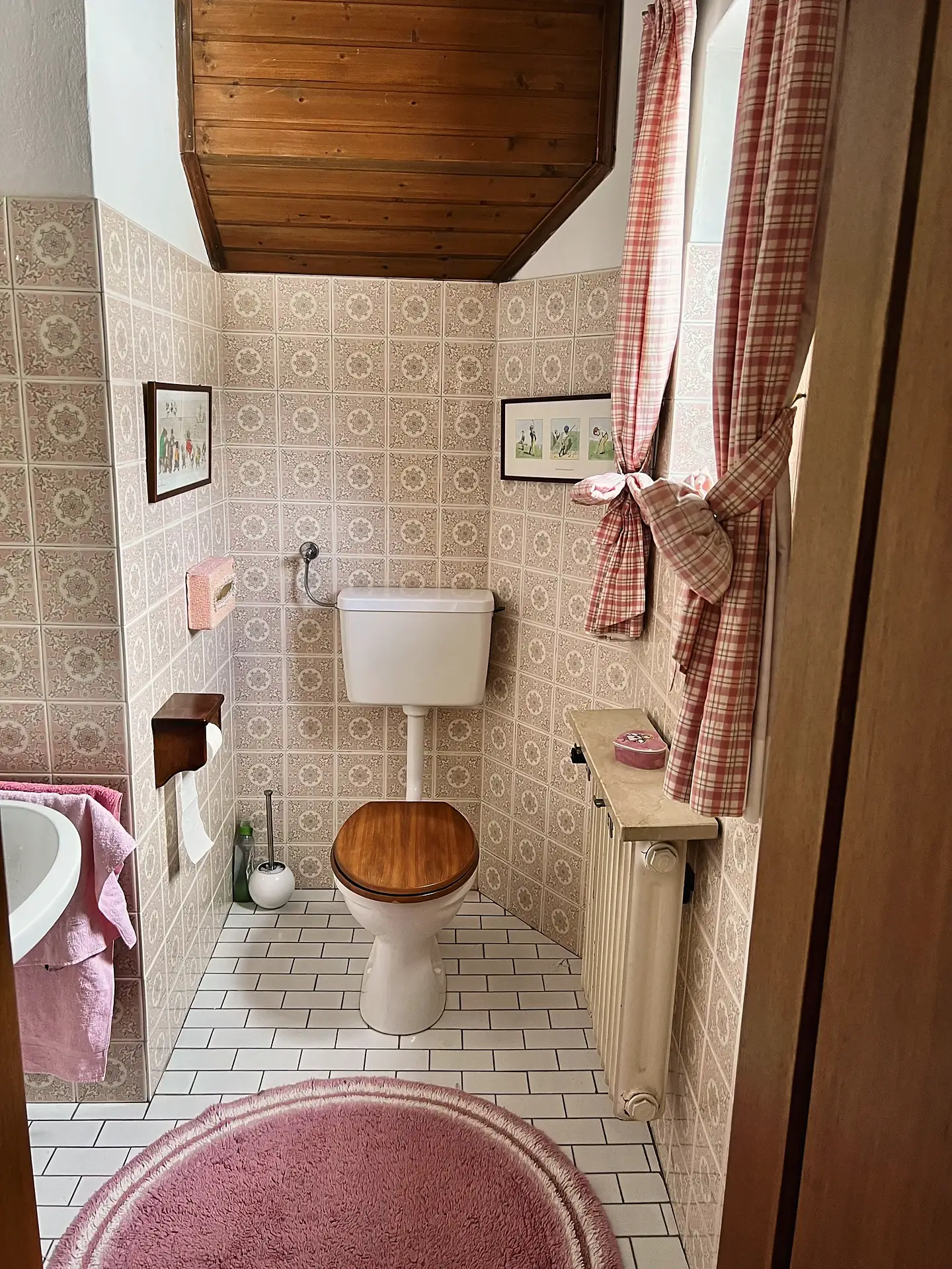 Kleines Gäste-WC mit gemusterten hellen Wandfliesen, Toilette mit Holzsitz und rot kariertem Vorhang.
