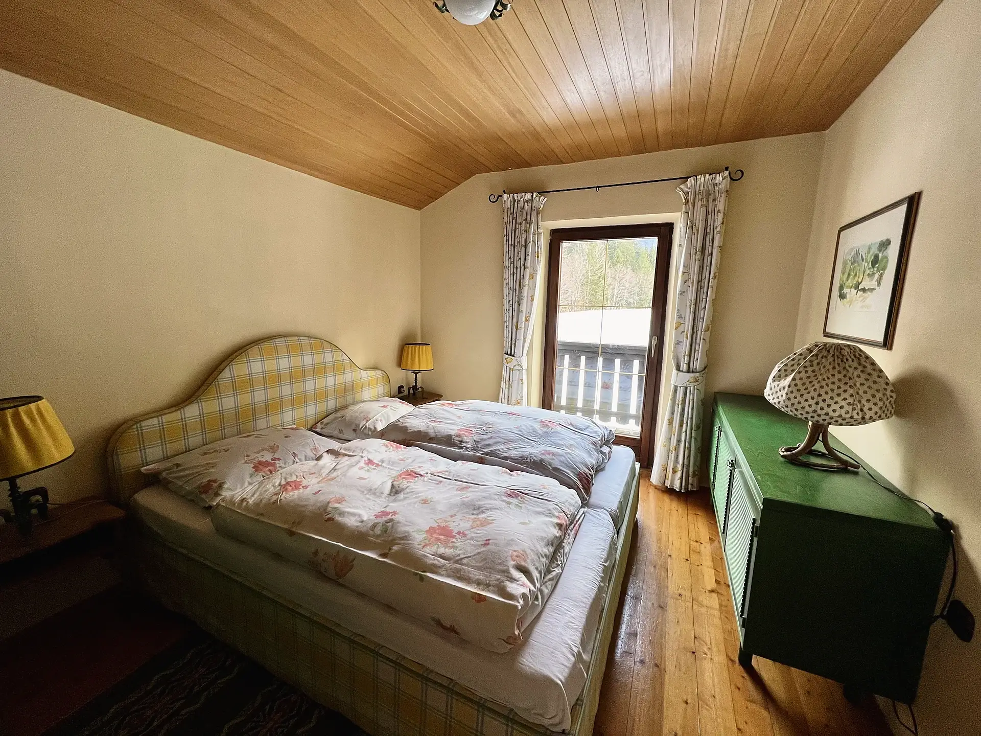 Schlafzimmer mit gelb kariertem Bett-Kopfteil, grüner Kommode und Balkontür.